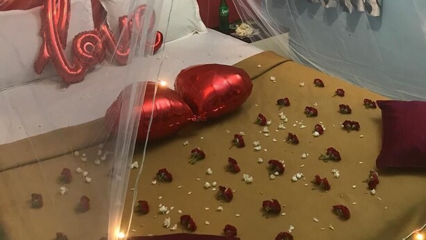Een kamer met een bed bedekt met rozenblaadjes, rode hartvormige ballonnen en een hemelbed.