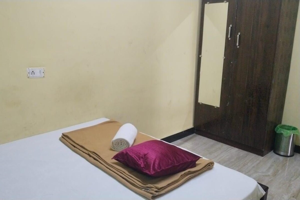 A small, simple room with a bed, a pillow, a rolled-up blanket, and a wardrobe.