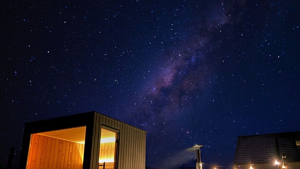 A wooden cabin with an open door, a small porch, and a string of lights.