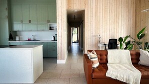 A spacious living area with a brown leather sofa, a white coffee table, and a kitchen visible through an open doorway.