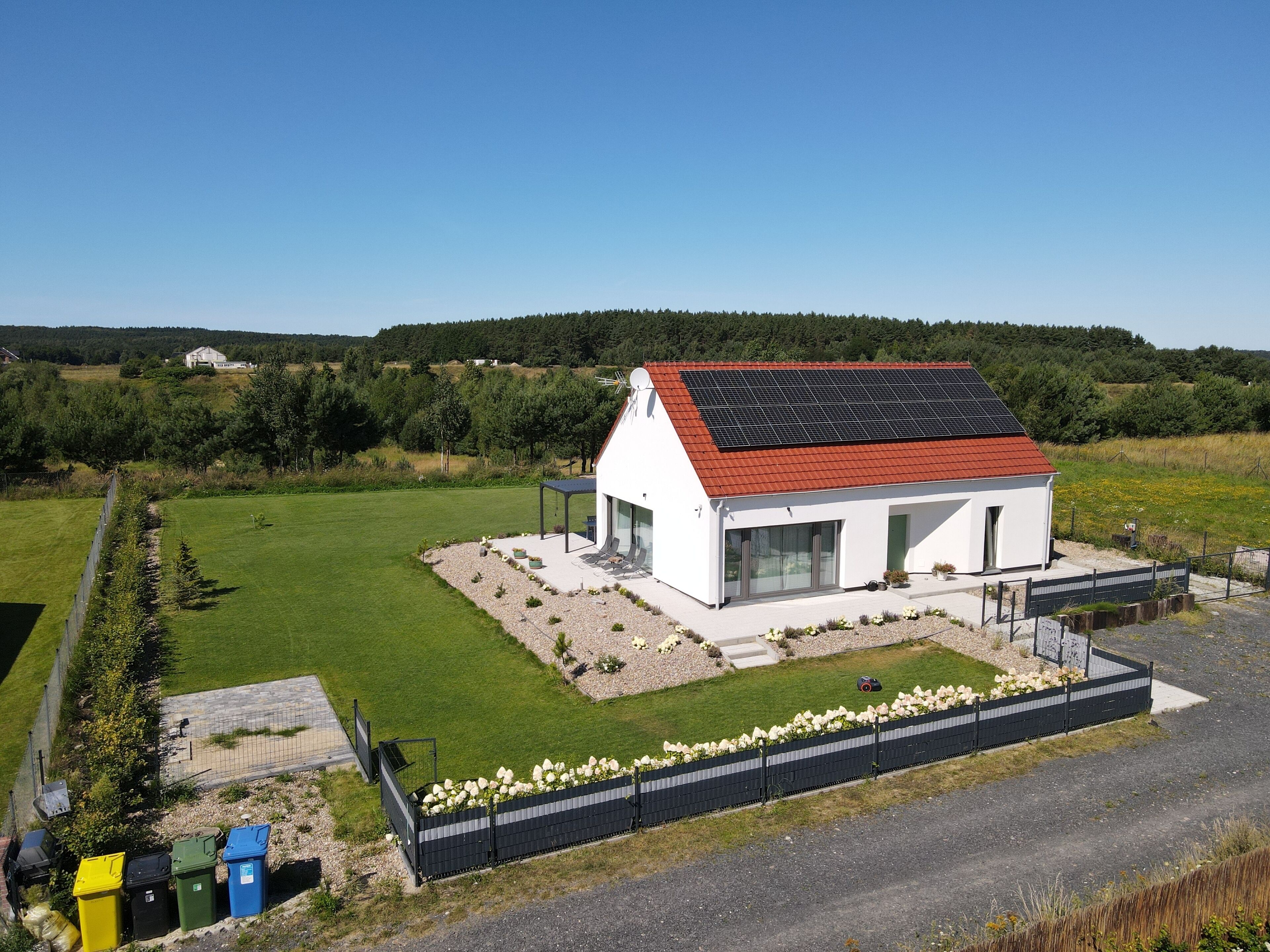 A modern house with a red roof, surrounded by a well-maintained lawn and a flower bed.