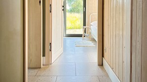 A hallway with wooden walls and a tiled floor leading to a room with a bed and a window.