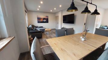 Ein modernes Wohnzimmer mit einer Couch, einem Esstisch und einem an der Wand befestigten Fernseher.