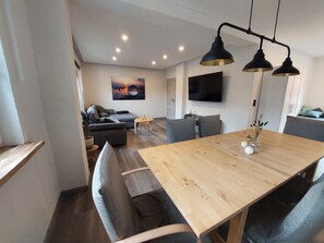 A modern living room with a sofa, a dining table, and a TV mounted on the wall.