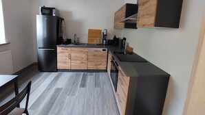 Une cuisine compacte équipée d’un réfrigérateur, de meubles en bois, d’un évier et d’un plan de travail agrémenté de divers appareils et ustensiles.