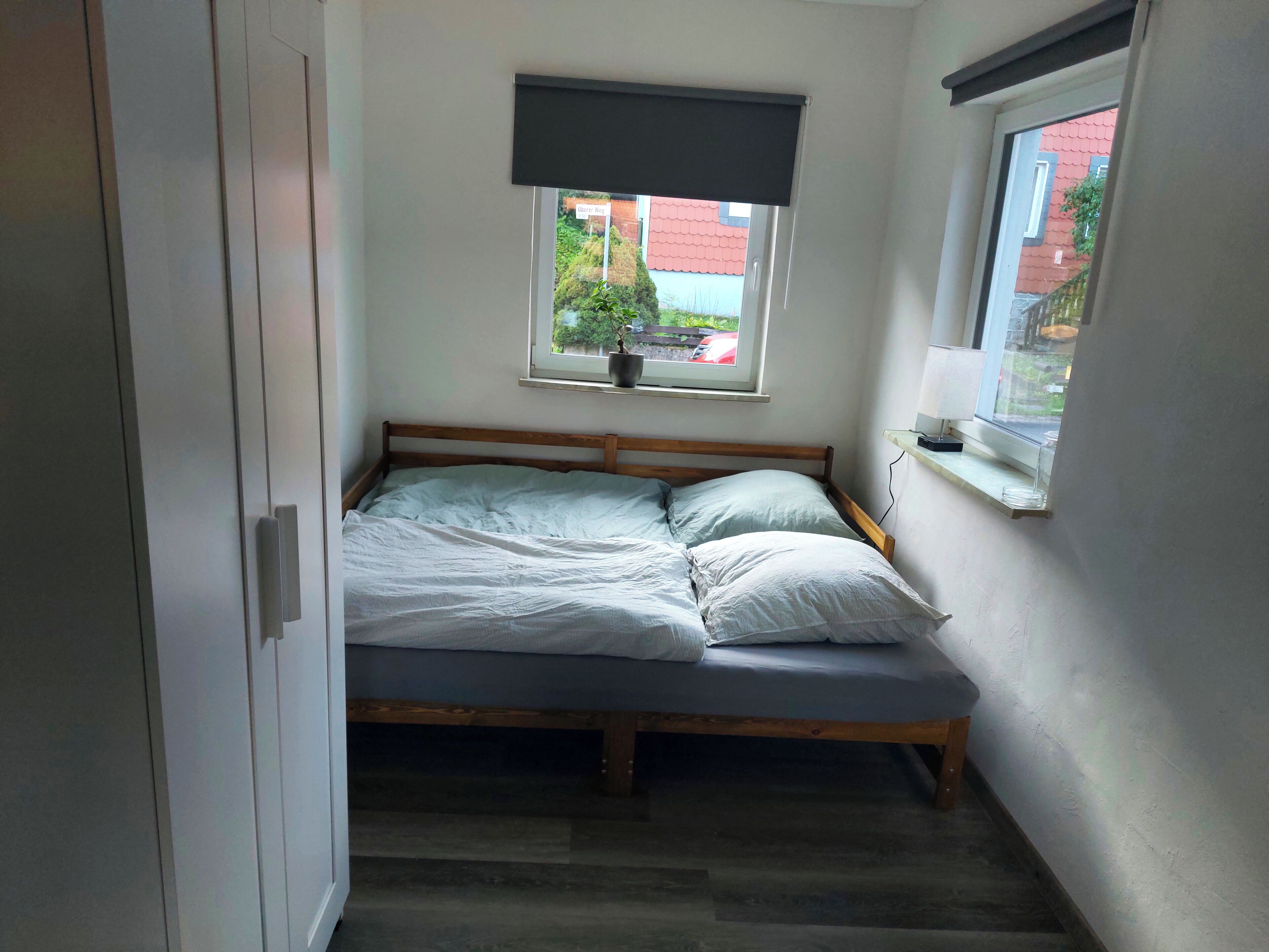 Ein kleines Schlafzimmer mit einem Einzelbett, einem Fenster mit Blick auf ein rotes Gebäude und einer Tür links.