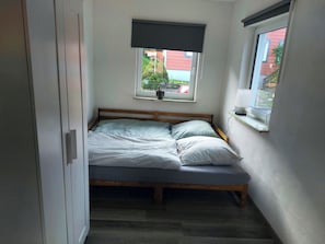 A small bedroom with a single bed, a window with a view of a red building, and a door on the left.