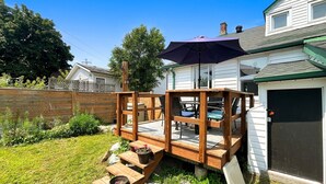 Une terrasse en bois avec une table et des chaises, un espace salon couvert et une porte de garage.