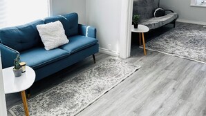 Un salon moderne avec un canapé bleu, un fauteuil gris, une petite table blanche et un tapis à motifs.