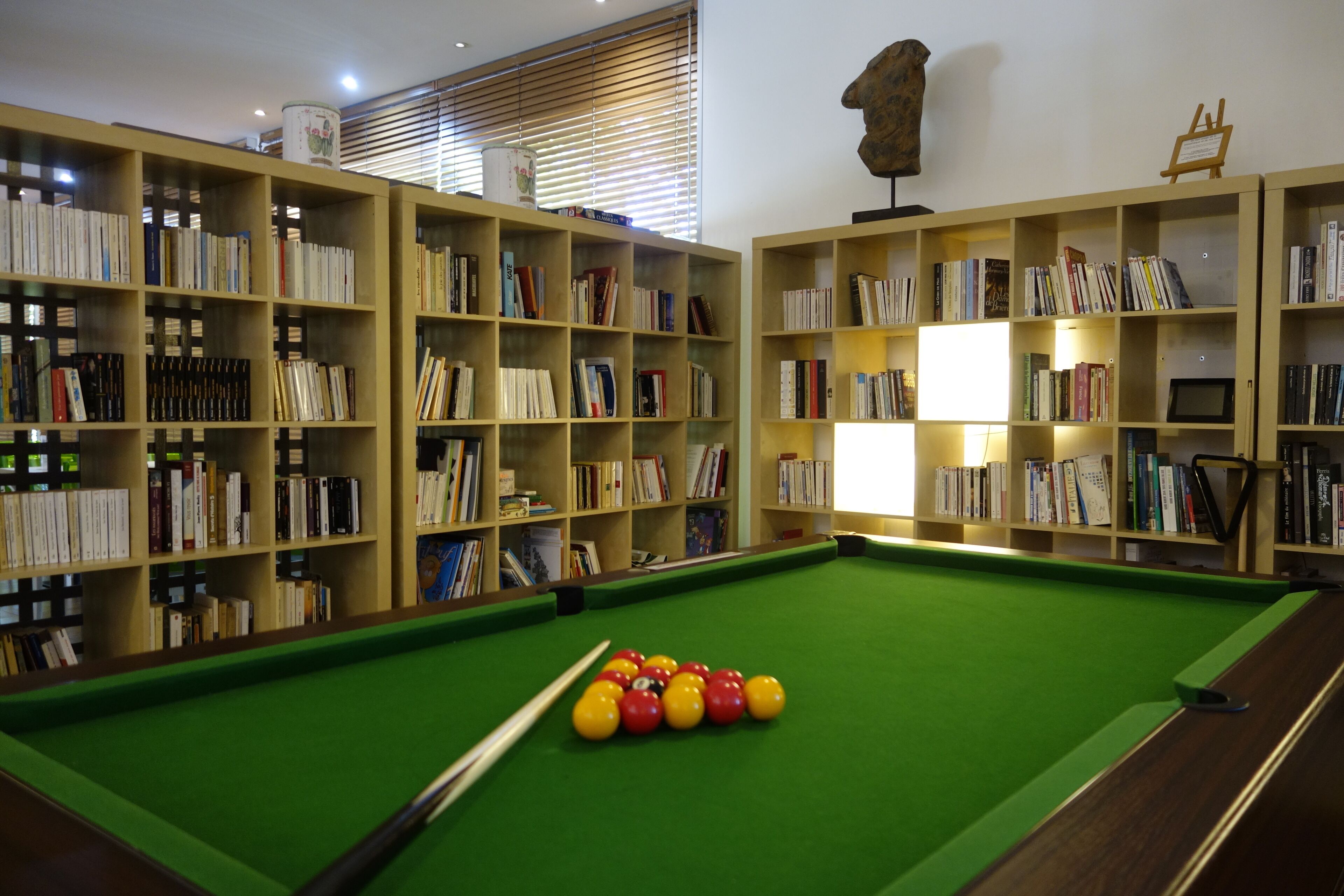 A pool table with balls in the center, surrounded by bookshelves filled with books.