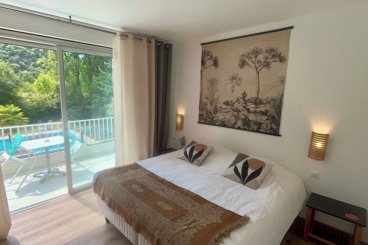 A bedroom with a large bed, a balcony with a pool, and a tropical mural on the wall.