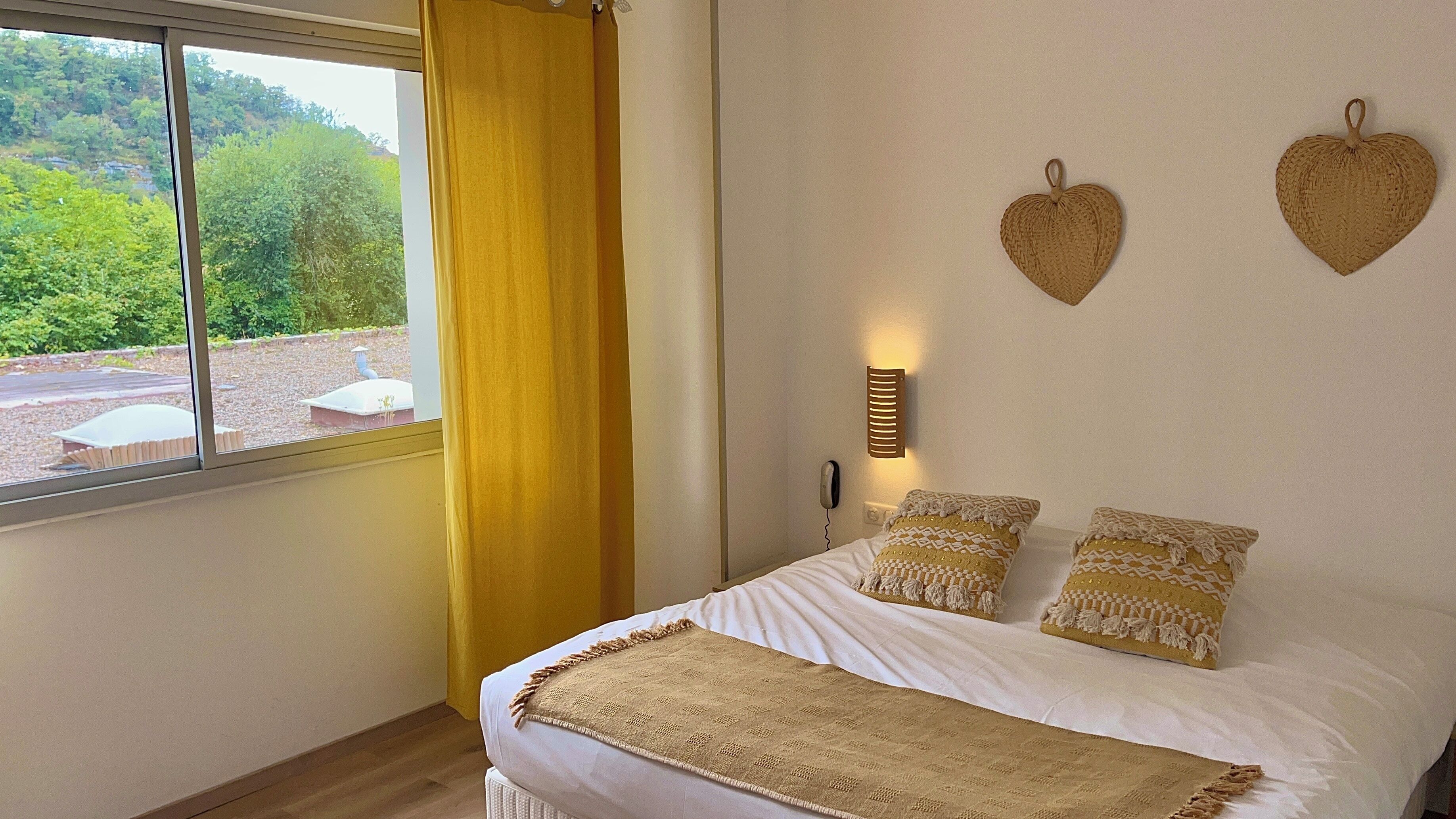 Un dormitorio con una cama, una ventana con cortinas amarillas y dos adornos en forma de corazón en la pared.