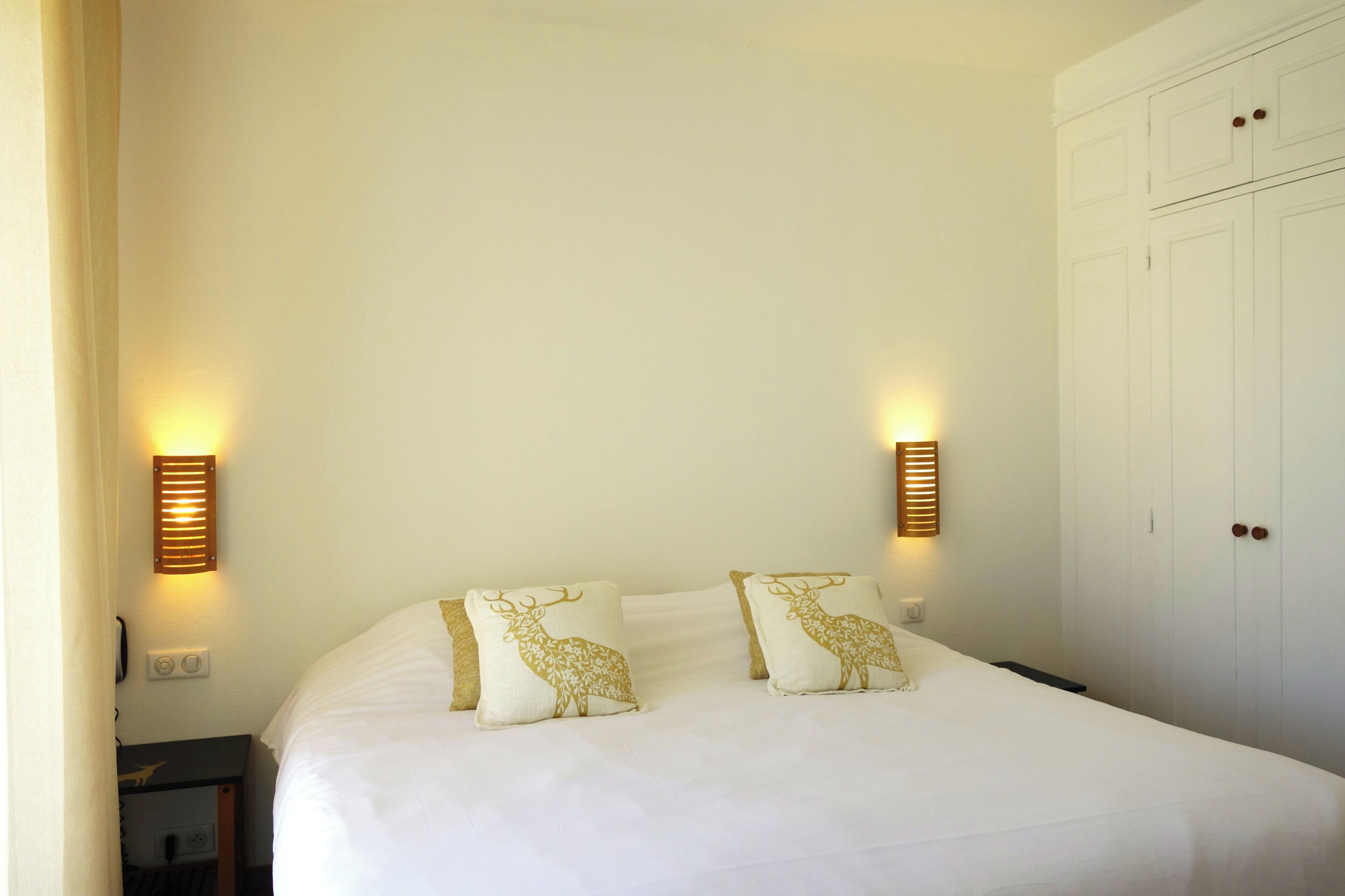 Habitació d'hotel amb llit, dues làmpades penjades a la paret i un armari.