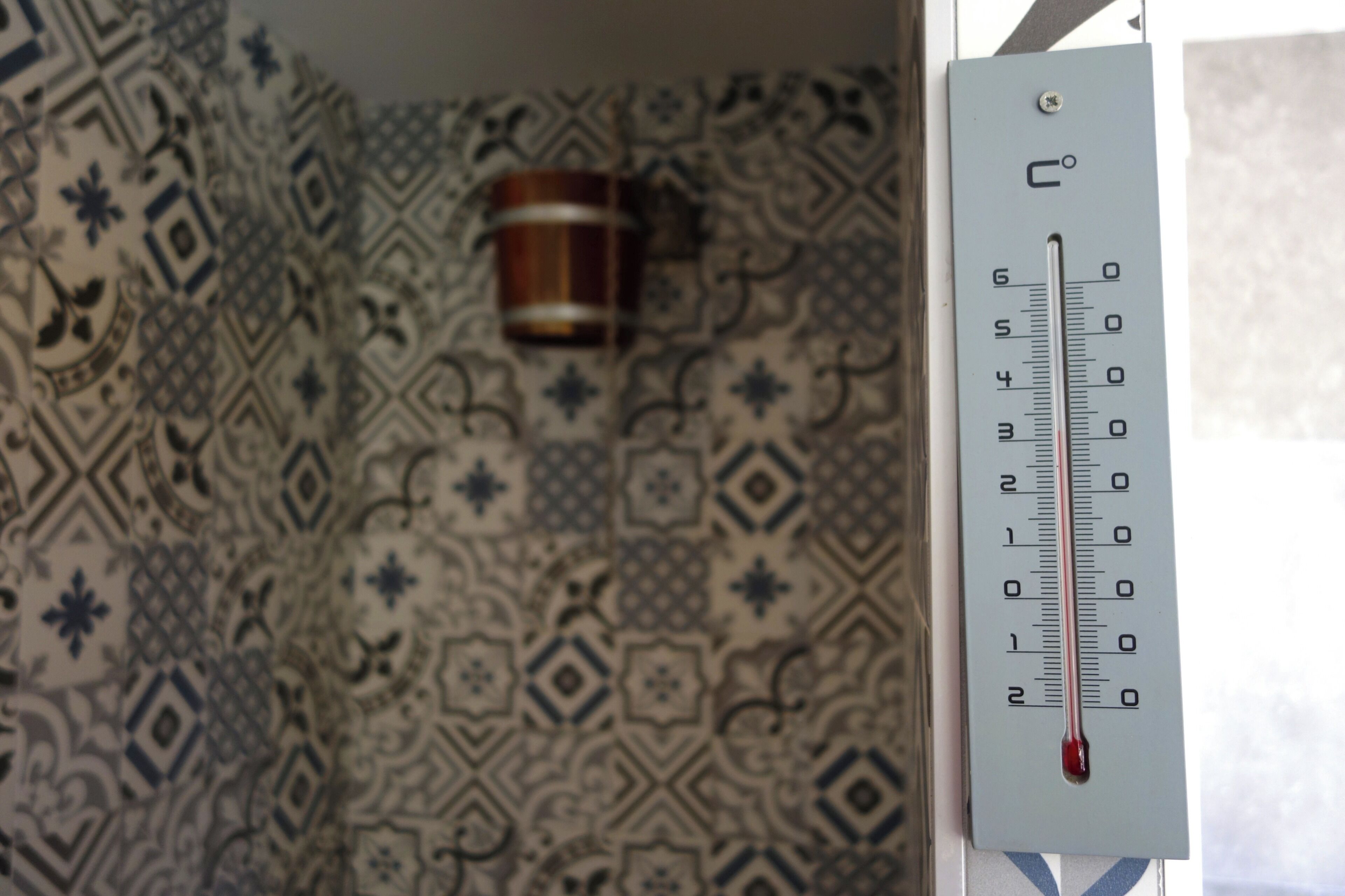Un termómetro que marca 2 grados Celsius, una pared con diseño y una taza colgada en la pared.