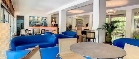 A modern hotel lobby with blue sofas, a round table, and a bar area.