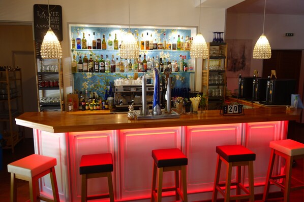 A bar area with a wooden counter, multiple stools, and a variety of bottles and glasses on shelves. - Hôtel La Ségalière Spa Bar (Cajarc)