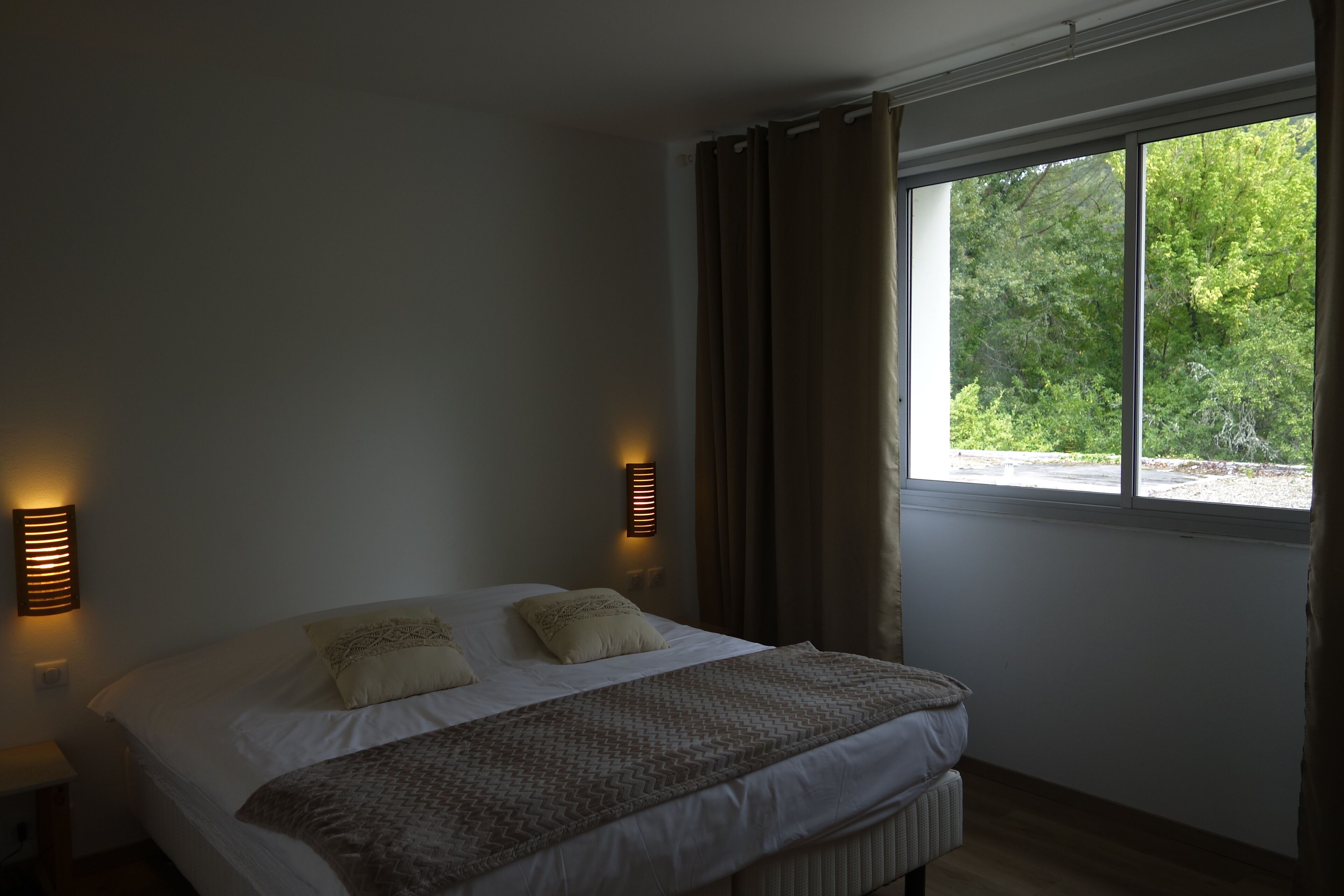 A bedroom with a large bed, two wall-mounted lights, a window with curtains, and a radiator.