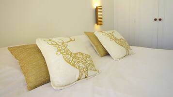 Una cama con dos almohadones decorativos con diseño de ciervo, una lámpara de pared y un armario blanco con tiradores de madera.