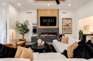 A modern living room with a fireplace, a mounted TV, and a sofa with cushions. - Ultra-Luxe Old Town Estate | Resort Pool + Spa (Scottsdale)