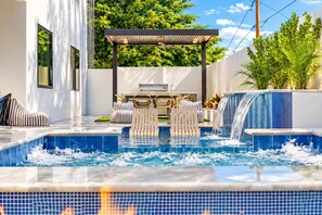 A modern outdoor pool area with a hot tub, lounge chairs, and a waterfall feature.