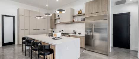 Una cocina moderna con una isla central, electrodomésticos de acero inoxidable e iluminación colgante.