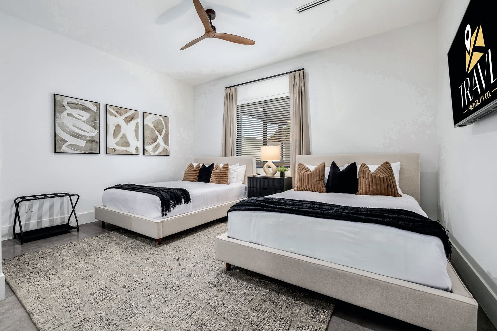Une chambre moderne avec deux lits, un ventilateur de plafond et des œuvres d’art accrochées au mur.