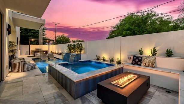 Een modern buitenzwembad met een jacuzzi, zitplaatsen en een vuurplaats.