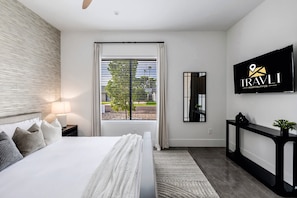 Una habitación de hotel moderna con una cama grande, un televisor montado en la pared y una ventana con persianas.