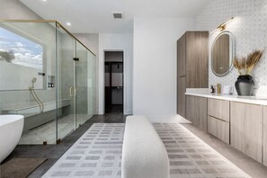 Un baño moderno con ducha envuelta en vidrio, una bañera blanca y un tocador de madera con espejo.