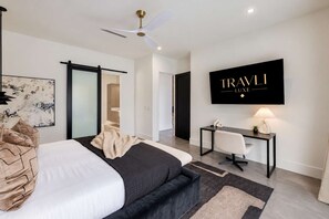 Moderni hotellihuone, jossa on sänky, työpöytä ja televisio, jolla näkyy kanava nimeltä ”TRAVEL LUXE”.