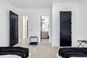 A modern hotel room with a large bed, a small seating area, a bathroom with a mirror, and a door leading to another room. - Ultra-Luxe Old Town Estate | Resort Pool + Spa (Scottsdale)