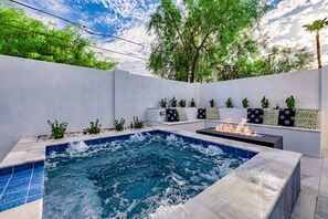Un jacuzzi con chimenea, rodeado por un muro blanco con plantas y asientos.