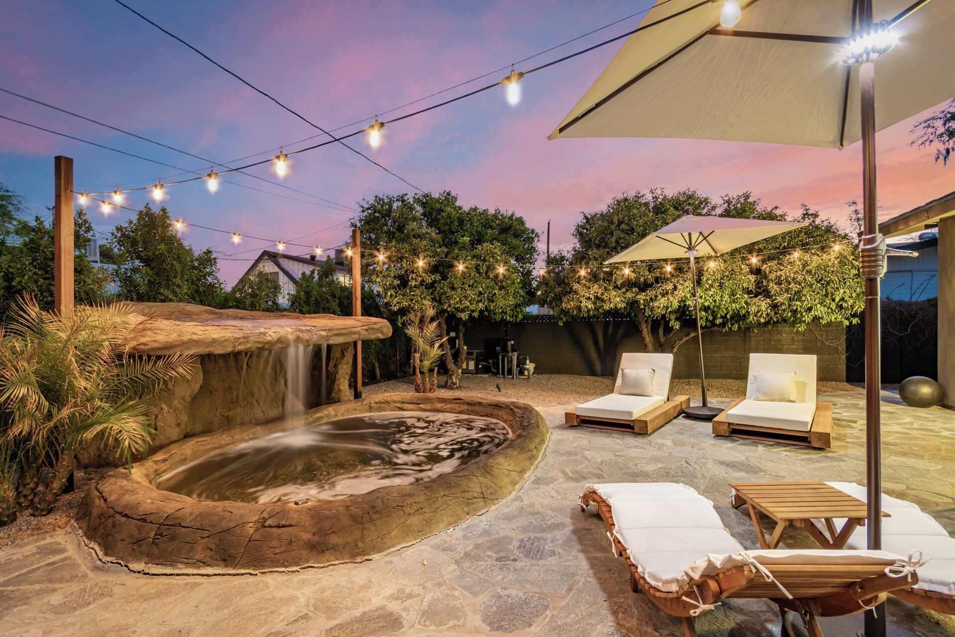 A backyard with a hot tub, lounge chairs, and string lights.