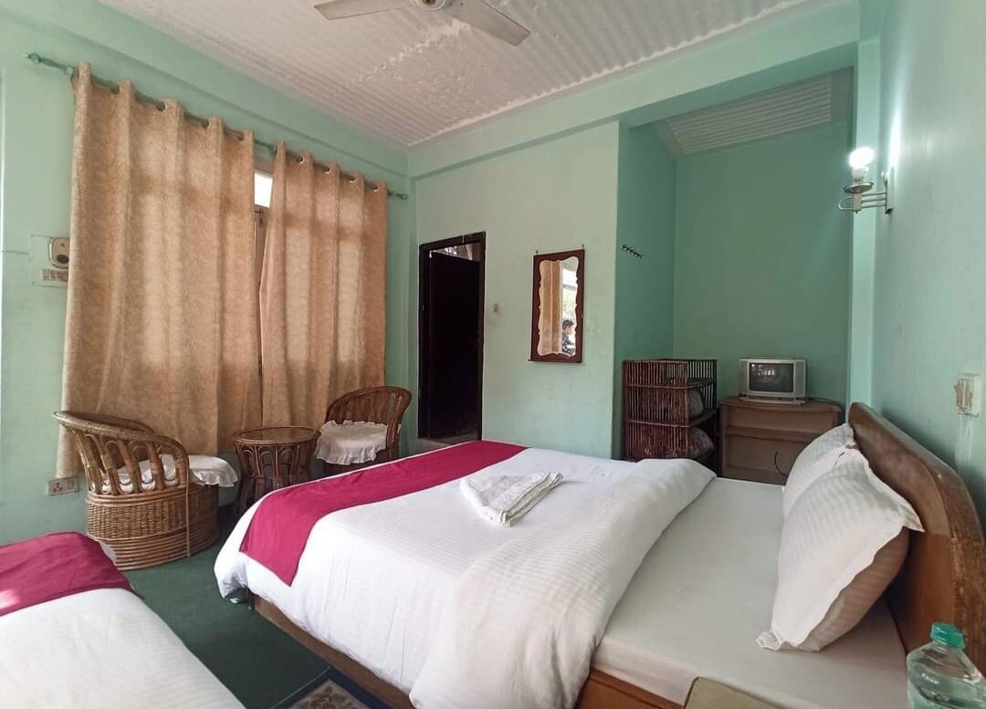 A room with two beds, a ceiling fan, a television, and a window with curtains.