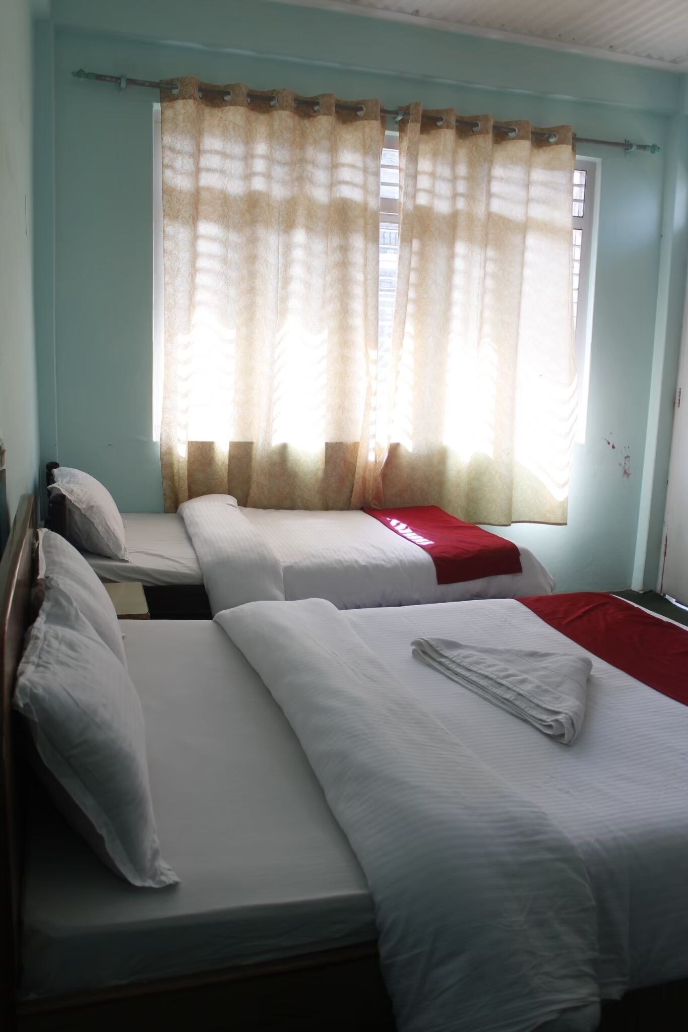 A room with two single beds, a window with a curtain, and a door.