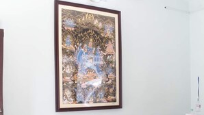 Une pièce comprenant deux chaises en bois, une table ronde et un tableau encadré accroché au mur.
