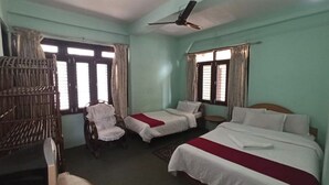 Une chambre d’hôtel avec deux lits simples, une chaise, un bureau et un ventilateur de plafond.