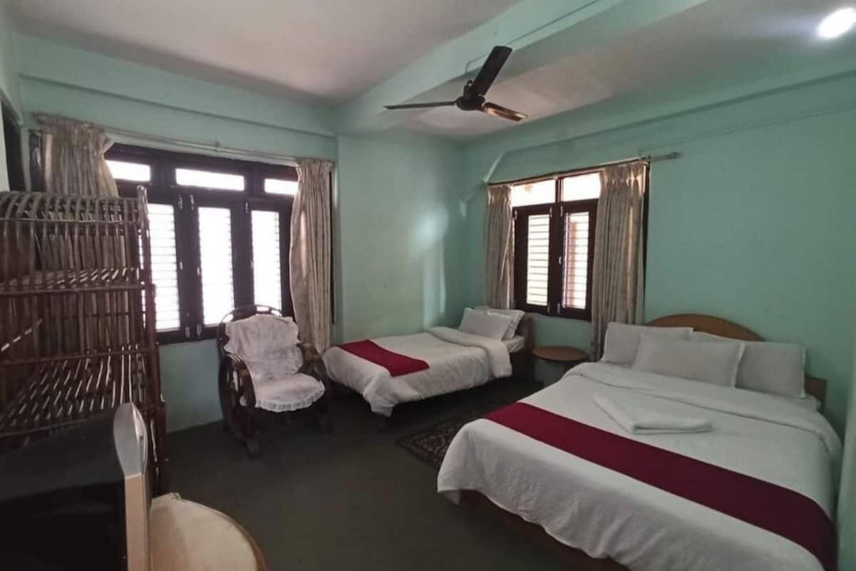 A hotel room with two single beds, a chair, a desk, and a ceiling fan.