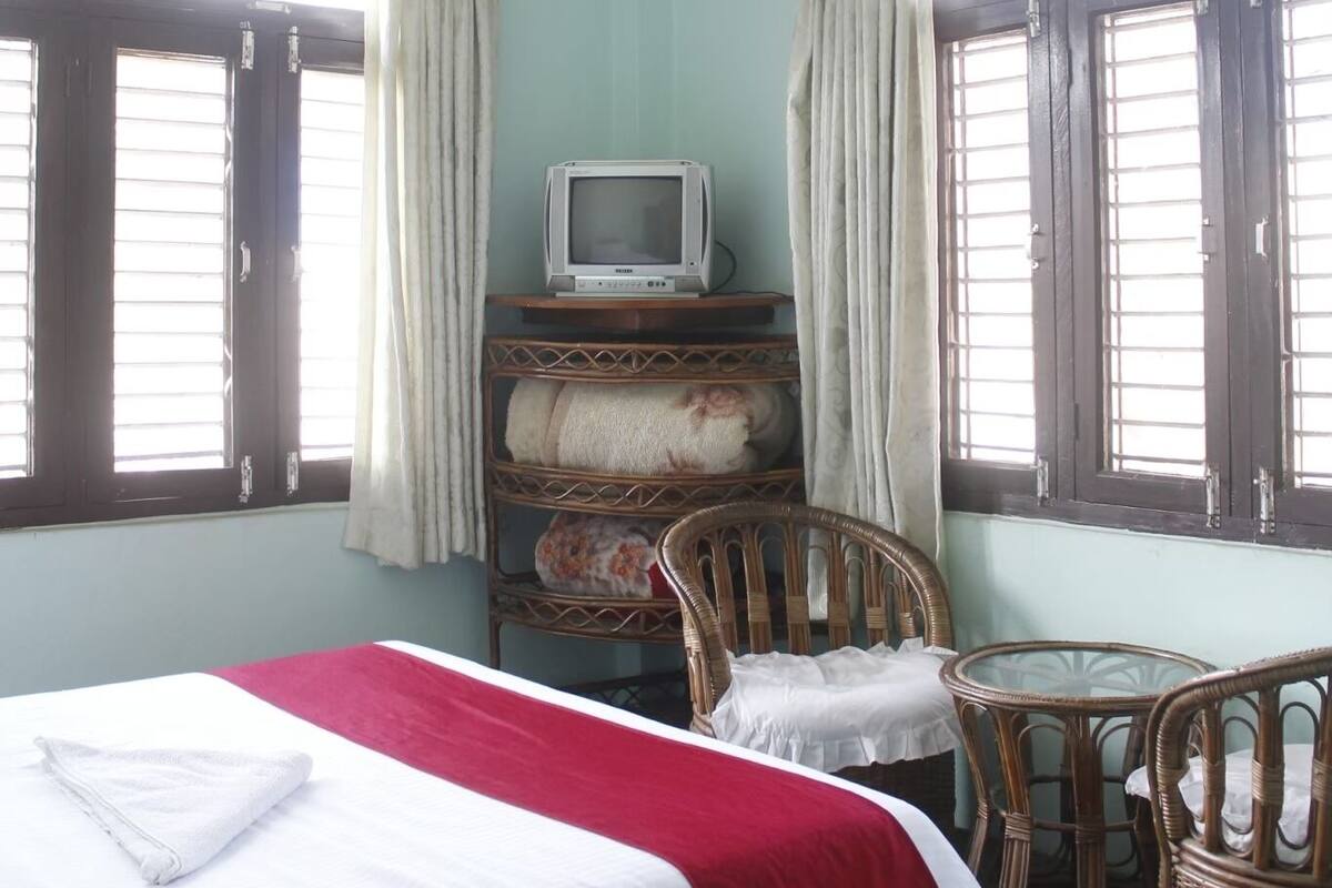 A room with a bed, a television, wicker chairs, and curtains.