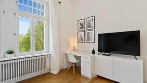 A modern room with a white desk, a flat-screen TV, and a radiator. - Spacious & Tranquil Room in Limpertsberg (Luxembourg)