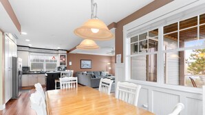 Une cuisine moderne avec des meubles blancs, une table à manger en bois et des luminaires suspendus.