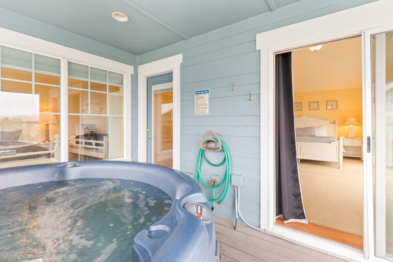 A hot tub on a wooden deck, a sliding glass door leading to a bedroom, and a safety sign on the wall.