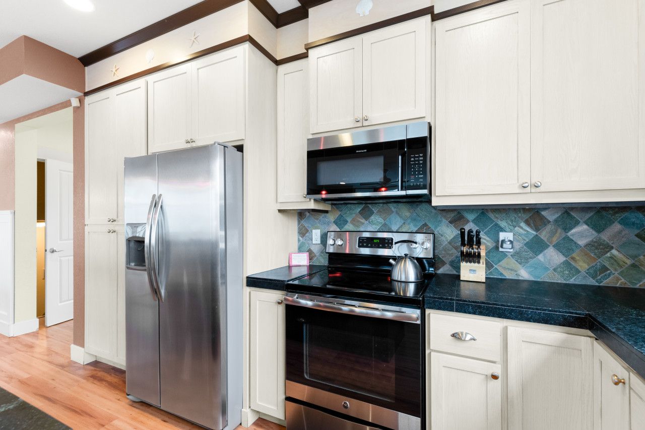 A modern kitchen with stainless steel appliances, white cabinetry, and a patterned backsplash.