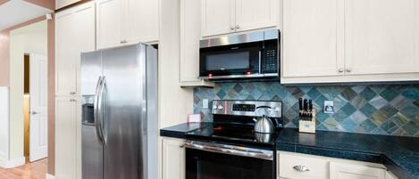 A modern kitchen with stainless steel appliances, white cabinetry, and a patterned backsplash.