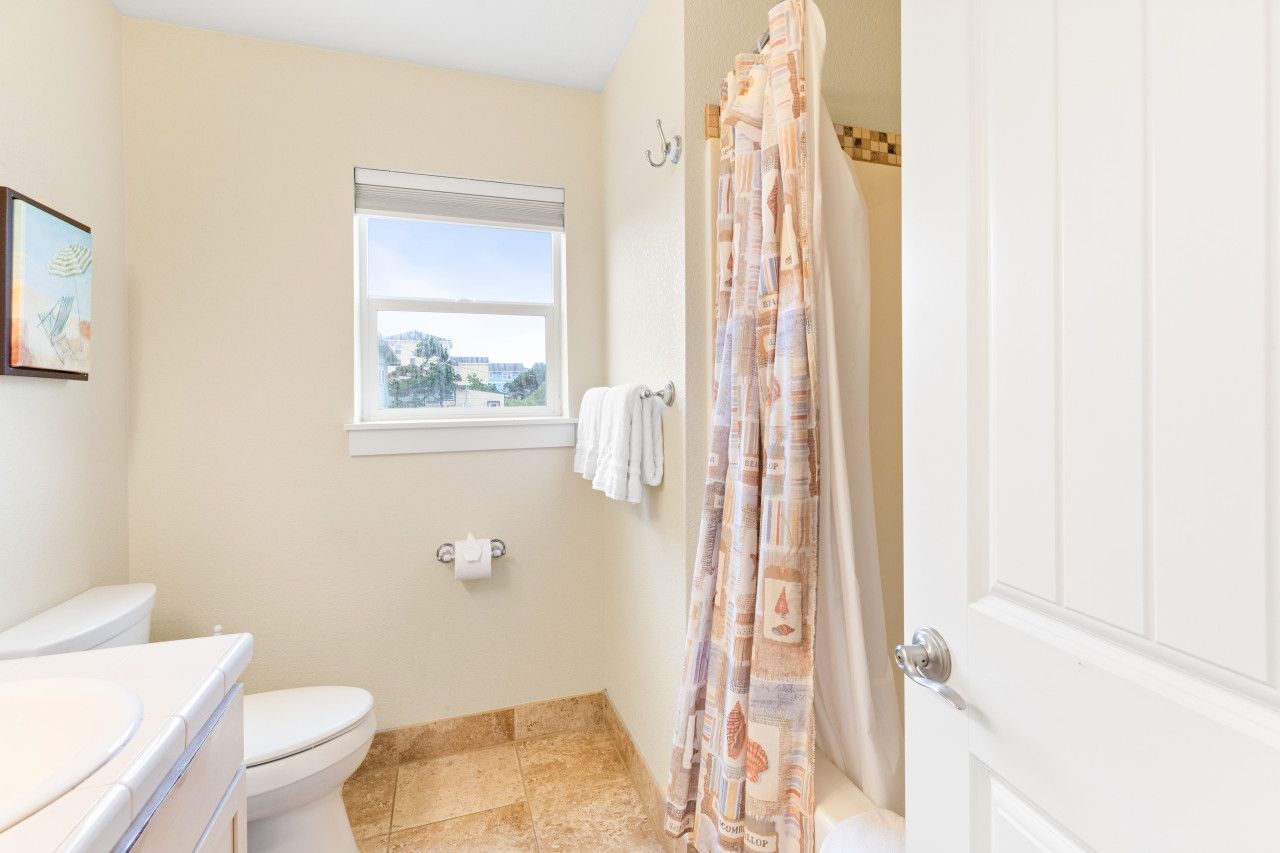 Un baño con inodoro, ventana, cortina de ducha y barra para toallas.