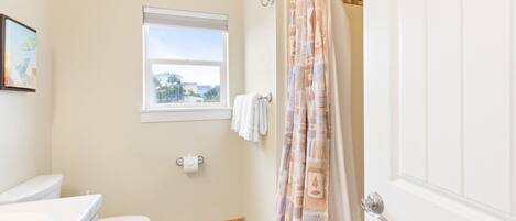 Un baño con inodoro, ventana, cortina de ducha y barra para toallas.