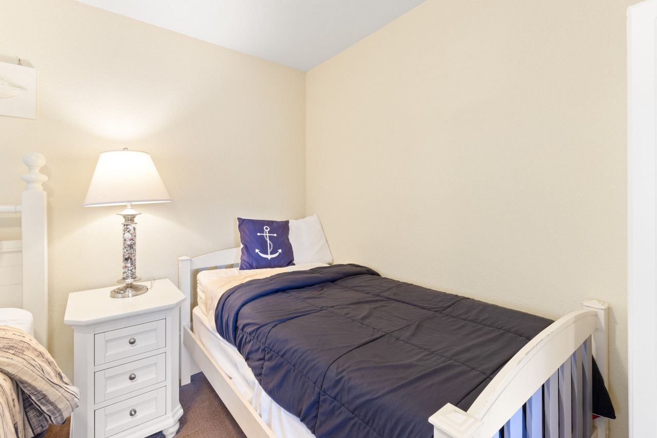 Un dormitorio con cama, una mesita de noche con lámpara, almohada con diseño de ancla y cómoda blanca.