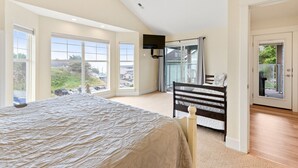 Une chambre avec un grand lit, un téléviseur fixé au mur et un balcon avec une chaise.