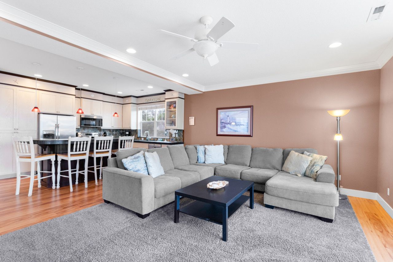 A modern living room with a gray sectional sofa, a black coffee table, and a dining area with white chairs.