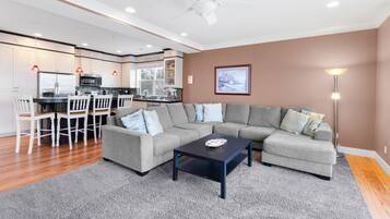 A modern living room with a gray sectional sofa, a black coffee table, and a dining area with white chairs.